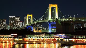 Uma ponte bem iluminada com duas torres e um rio com barcos.