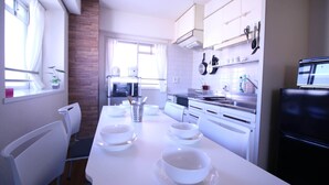 Eine moderne Küche mit weißen Schränken, einem langen Esstisch gedeckt mit Schüsseln, und einem Kühlschrank.
