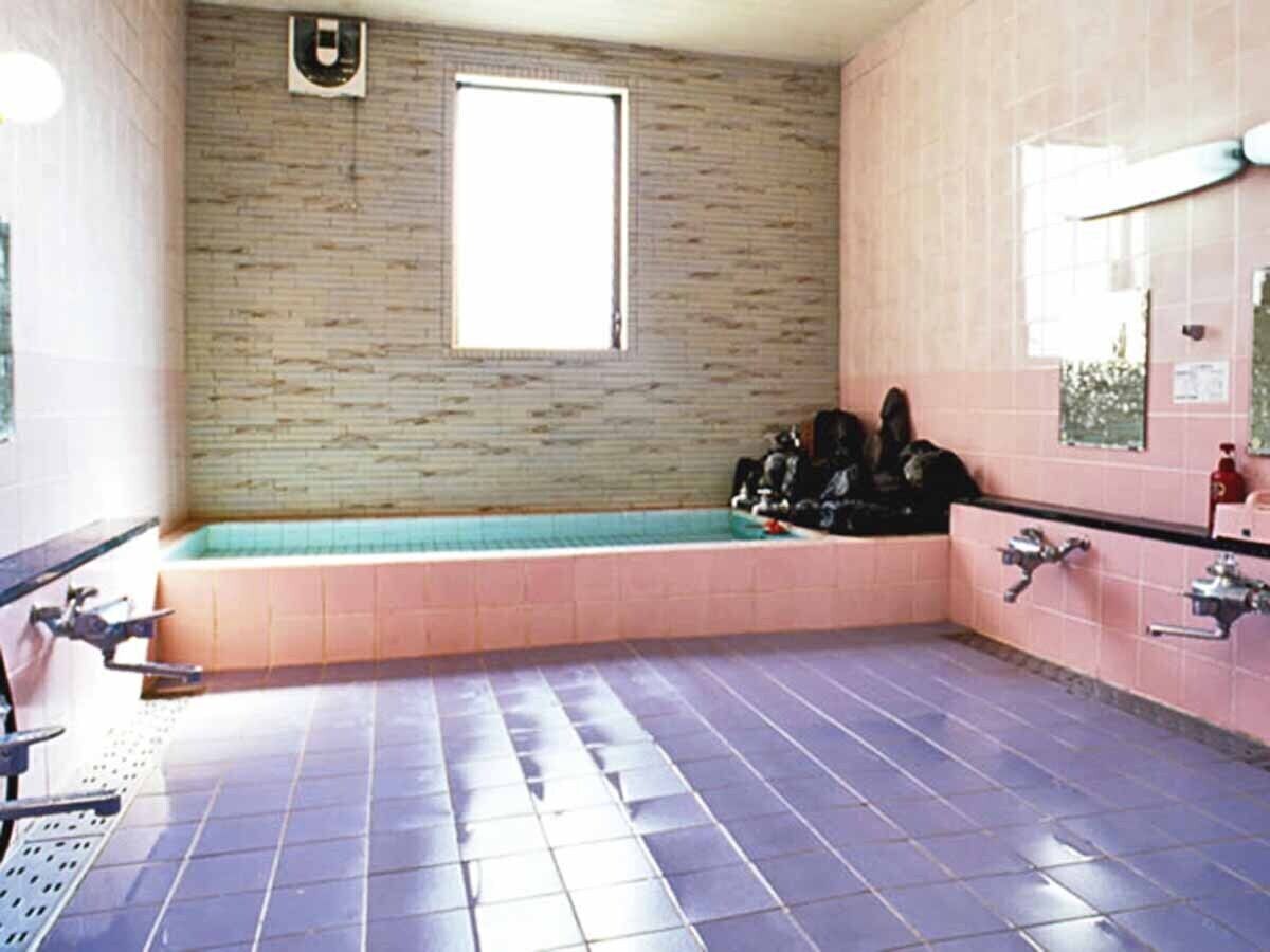 Une salle de bain avec une baignoire, une fenêtre et un carrelage au sol.