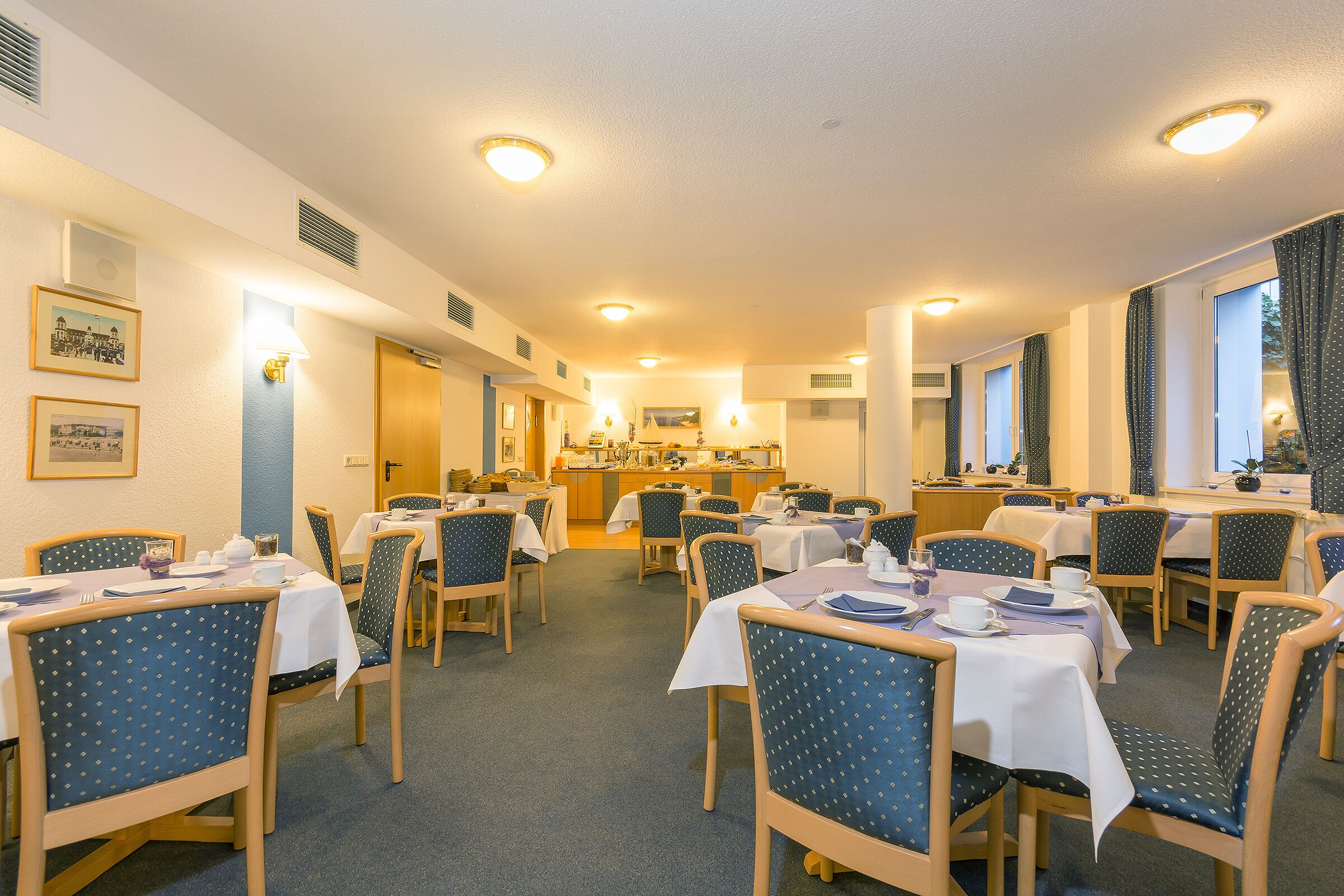 A dining area with tables set for meals, chairs, and a kitchen in the background.