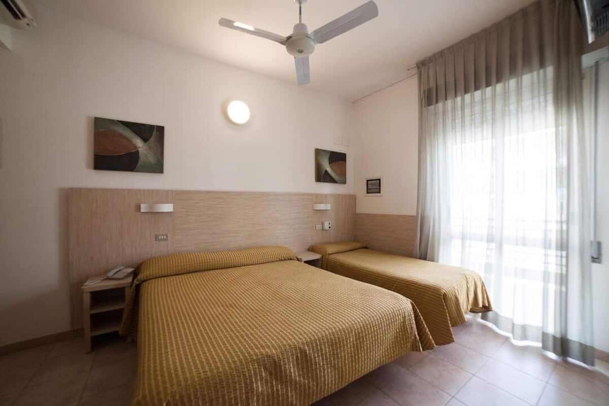 A hotel room with two beds, a ceiling fan, a bedside table with a phone, and artwork on the walls.