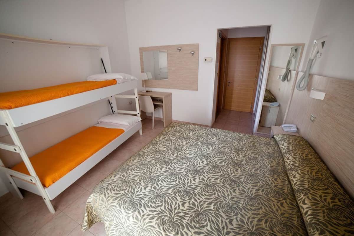 A room with bunk beds, a desk, a mirror, and a shower area.