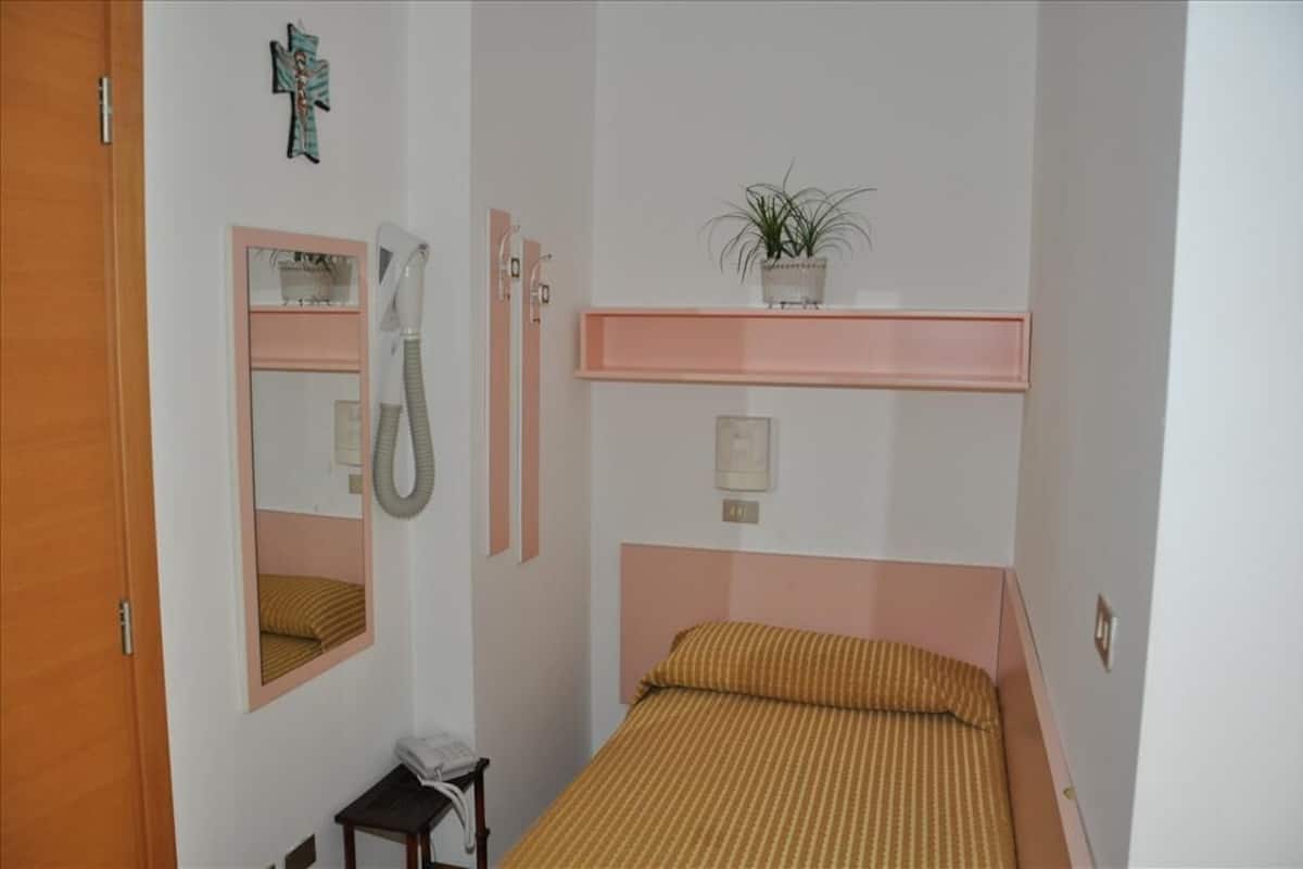 A bedroom with a bed, a mirror, a shelf with a plant, and a small table with a telephone.