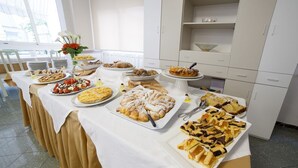 Una mesa de bufé con diversos postres y pasteles, ubicada en una habitación con armarios blancos y un ventanal.