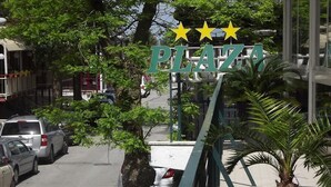 Señal que dice 'PLAZA' con tres estrellas, rodeada de coches aparcados y árboles.