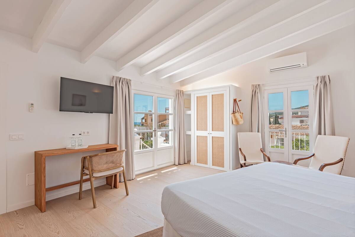 Quarto de hotel com cama, escrivaninha, cadeira e televisão.