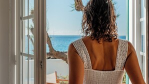 Una persona vestida de blanco parada frente a una puerta abierta, con vista a la playa y al océano.