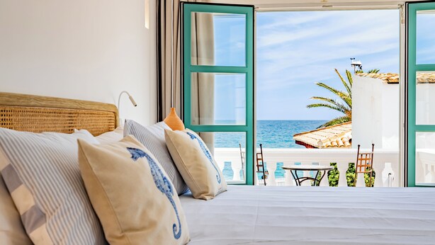 A bedroom with a large bed, a view of the sea, and an open door leading to a balcony with outdoor furniture. - The Sea Club (Capdepera)
