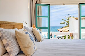 Un dormitorio con una cama grande, vista al mar y una puerta abierta que da a un balcón con mobiliario exterior.