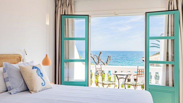 Un dormitorio con cama, almohadas y vista al mar a través de puertas abiertas.