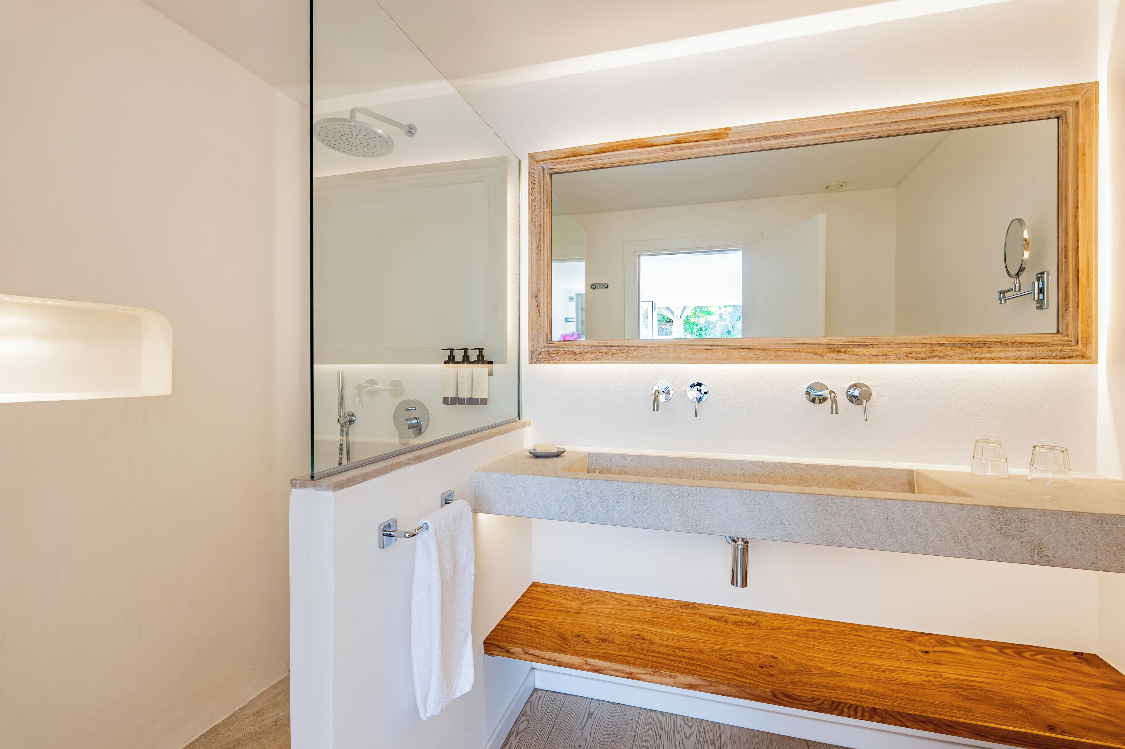 A modern bathroom with a large mirror, a wooden vanity, a shower, and a towel rack.