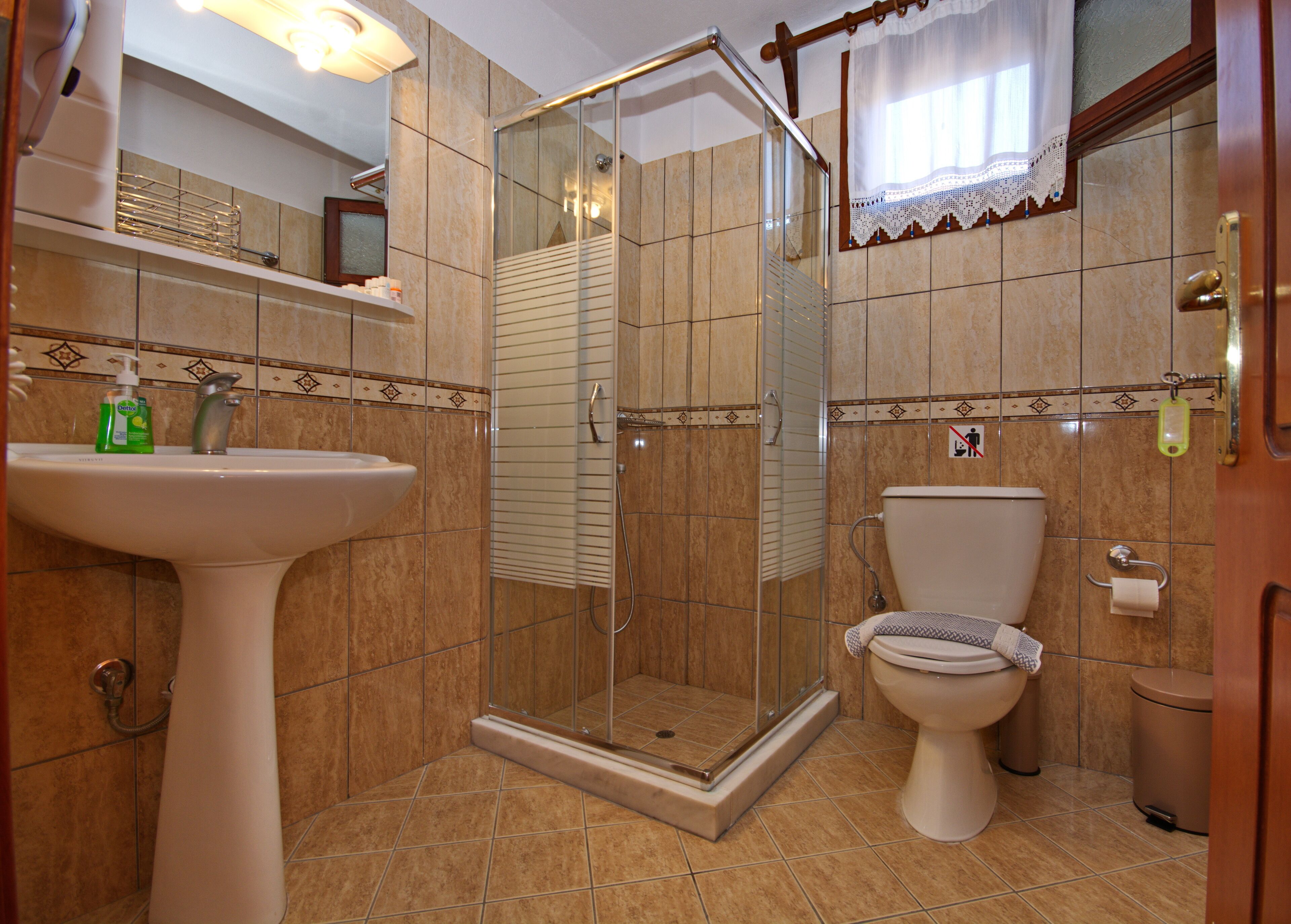 A bathroom with a glass-enclosed shower, a pedestal sink, and a toilet.