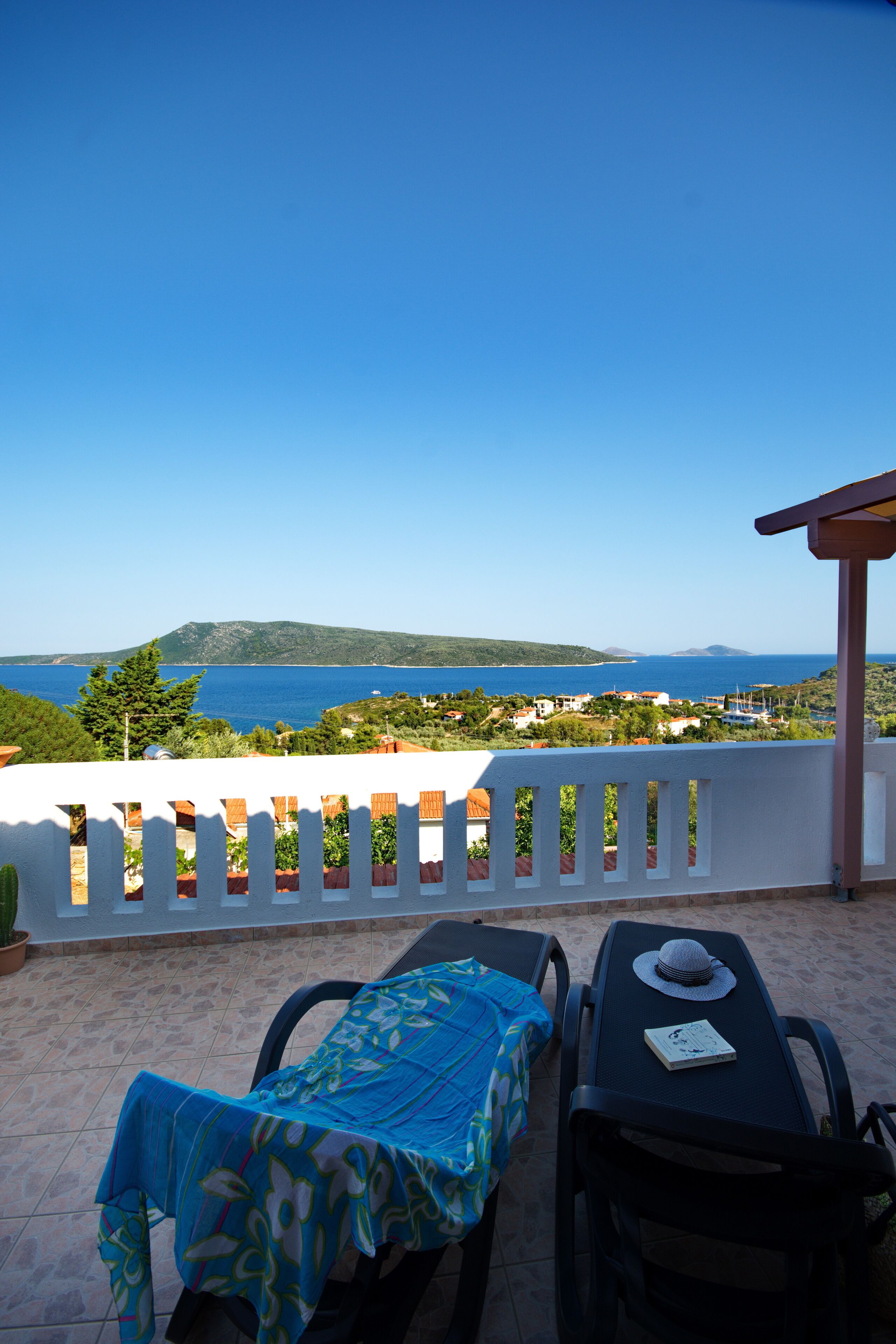 A balcony with a view of the sea, a table with a hat, and a chair.