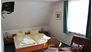 A hotel room with a bed, two bedside tables, a chair, a small table, a TV mounted on the wall, and a window with curtains. - Zum Harzer Jodlermeister (Thale)