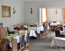 Un comedor con varias mesas y sillas, manteles blancos y un cuadro en la pared.