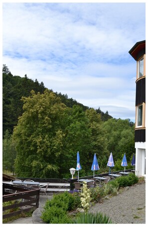 A terrace with outdoor seating, a mountain backdrop, and a building with a dark facade. - Zum Harzer Jodlermeister (Thale)