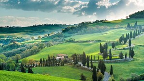 A rural landscape with rolling hills, a winding road, and a house surrounded by trees. - Bertusi Source- The Sunset (Pienza)