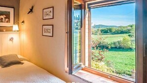 A bedroom with a large window, a bed, and a nightstand. - Bertusi Source- The Sunset (Pienza)