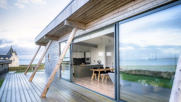 A modern house with a deck, a dining area, and a kitchen with a view of the sea.