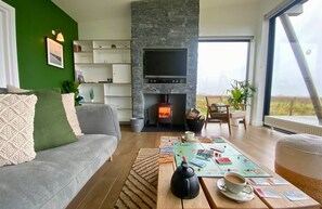 A modern living room with a stone fireplace, a flat-screen TV, and a view of the outdoors.