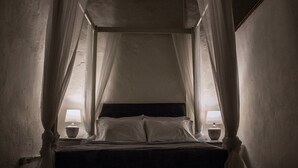 A dimly lit room with a bed under a canopy, two bedside tables with lamps, and a view through the canopy. - Relaxing Getaway in a Colonial Hotel
 (Zona colonial)