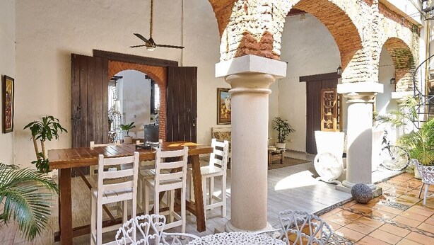 An outdoor dining area with a wooden table and white chairs, surrounded by arches and potted plants. - Relaxing Getaway in a Colonial Hotel
 (Zona colonial)
