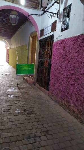A corridor with a brick floor, a green signboard, a metal gate, and a pink wall. - Dar Tsouli (Rabat)