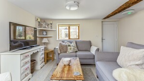 A living room with a television, sofa, coffee table, and a window with blinds. - Woodcut Cottage, Free WiFi, Rural Location (Evesham)
