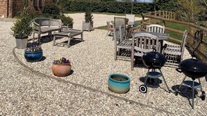 A gravel patio with outdoor furniture, a barbecue grill, and potted plants. - Woodcut Cottage, Free WiFi, Rural Location (Evesham)