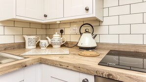 A kitchen with white cabinets, a wooden countertop, and a black induction cooktop. - Railway Cottage: Cosy Cotswolds Farm Retreat (Evesham)