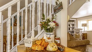 A wooden table with pastries, a vase of flowers, and a sign reading "Don't let the cat half asleep." - Railway Cottage: Cosy Cotswolds Farm Retreat (Evesham)