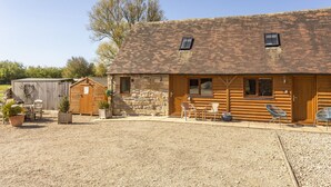 A rustic wooden building with a gravel driveway, two small windows, and a wooden door. - Railway Cottage: Cosy Cotswolds Farm Retreat (Evesham)