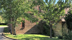 Ein Steinhaus mit Ziegeldach, umgeben von einer grünen Fläche und Bäumen.