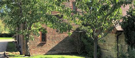 A stone building with a brick roof, surrounded by a grassy area and trees.