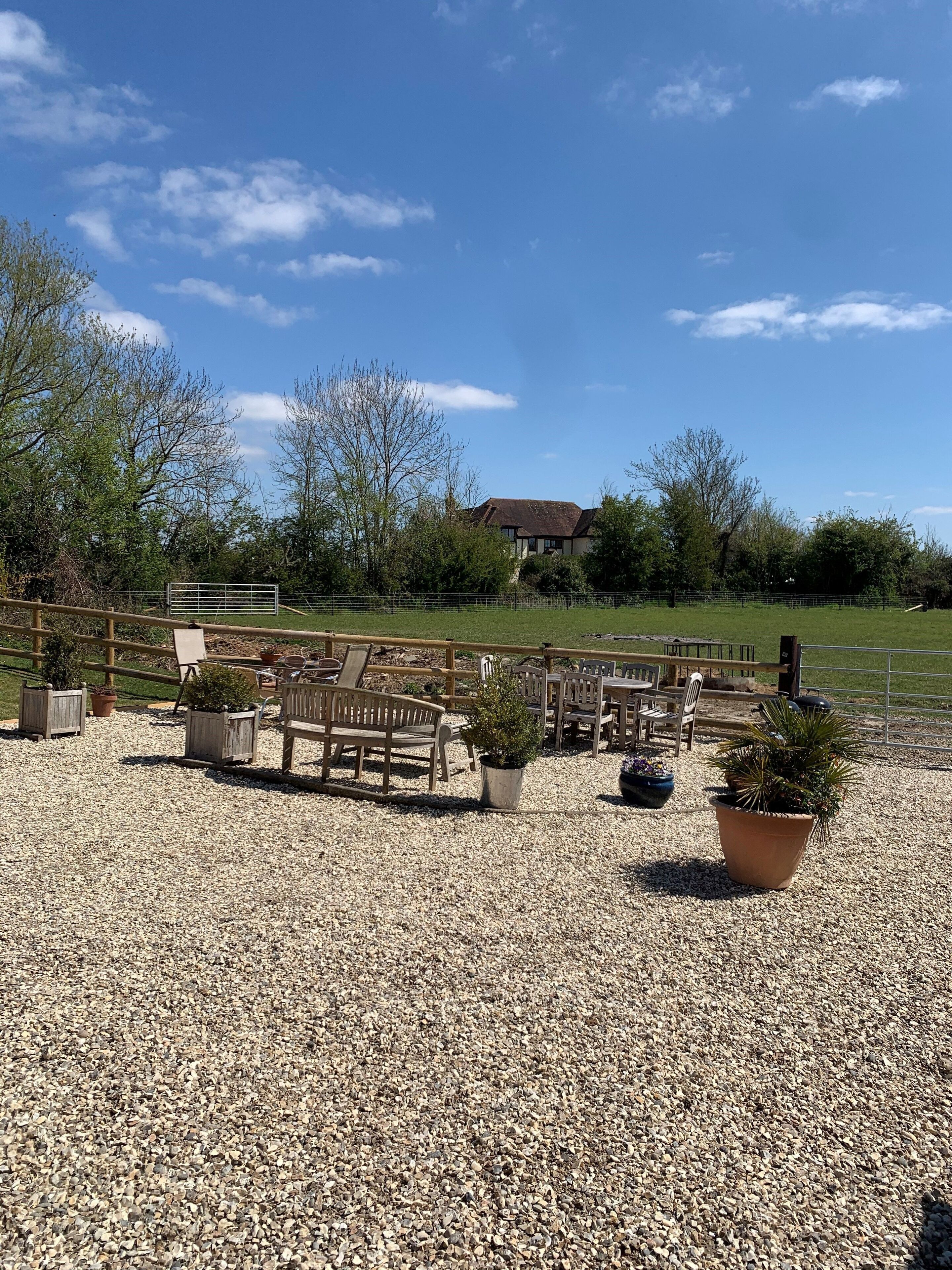 A gravel patio with wooden furniture and potted plants.