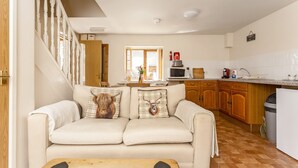 Ein gemütliches Wohnzimmer mit einer Couch, einem Holztisch und einer Küchenzeile mit Holzschränken und einer Mikrowelle.
