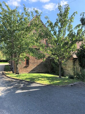 Un bâtiment en pierre, surmonté d’un toit en briques, entouré d’une pelouse et d’arbres.