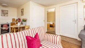 A cozy living room with a striped sofa, a dining area with a table and chairs, and a kitchen with an oven and a sink. - Farm End Cottage - sleeps 2 guests  in 1 bedroom (Evesham)