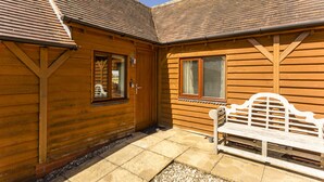 A wooden cabin with a tiled patio and a white bench. - Farm End Cottage - sleeps 2 guests  in 1 bedroom (Evesham)