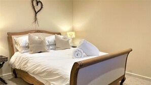 A neatly made bed with a wooden frame, white bedding, and a rolled towel on the side. - Farm End Cottage - sleeps 2 guests  in 1 bedroom (Evesham)