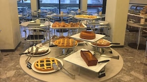 Un espace buffet où diverses sortes de desserts sont présentées sur des présentoirs à étages, entouré de chaises et de tables en métal.