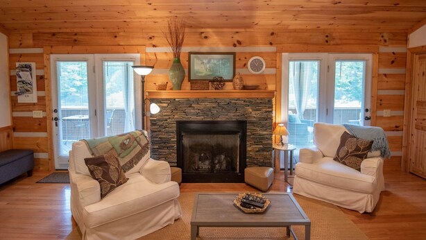A cozy cabin interior with two sofas, a fireplace, and a stone wall. - Firefly Fields | Minutes to Blue Ridge Parkway | Hot Tub & Screened Porch (Fleetwood)