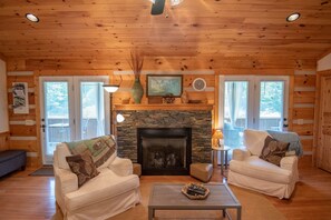 A cozy cabin interior with two sofas, a fireplace, and a stone wall. - Firefly Fields | Minutes to Blue Ridge Parkway | Hot Tub & Screened Porch (Fleetwood)
