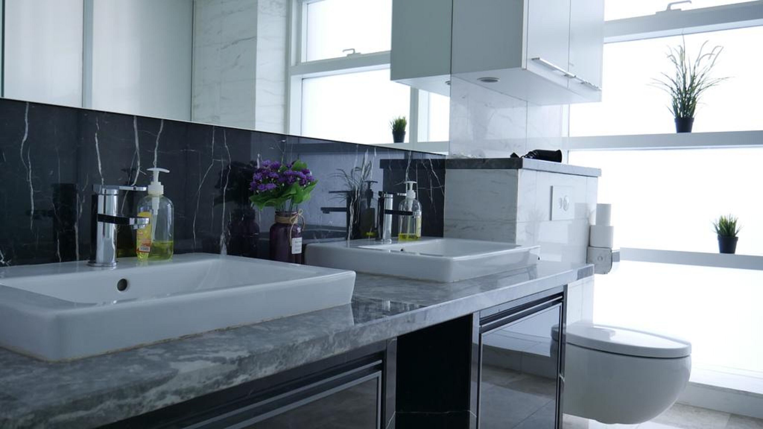 A modern bathroom with two sinks, a toilet, and a large mirror.
