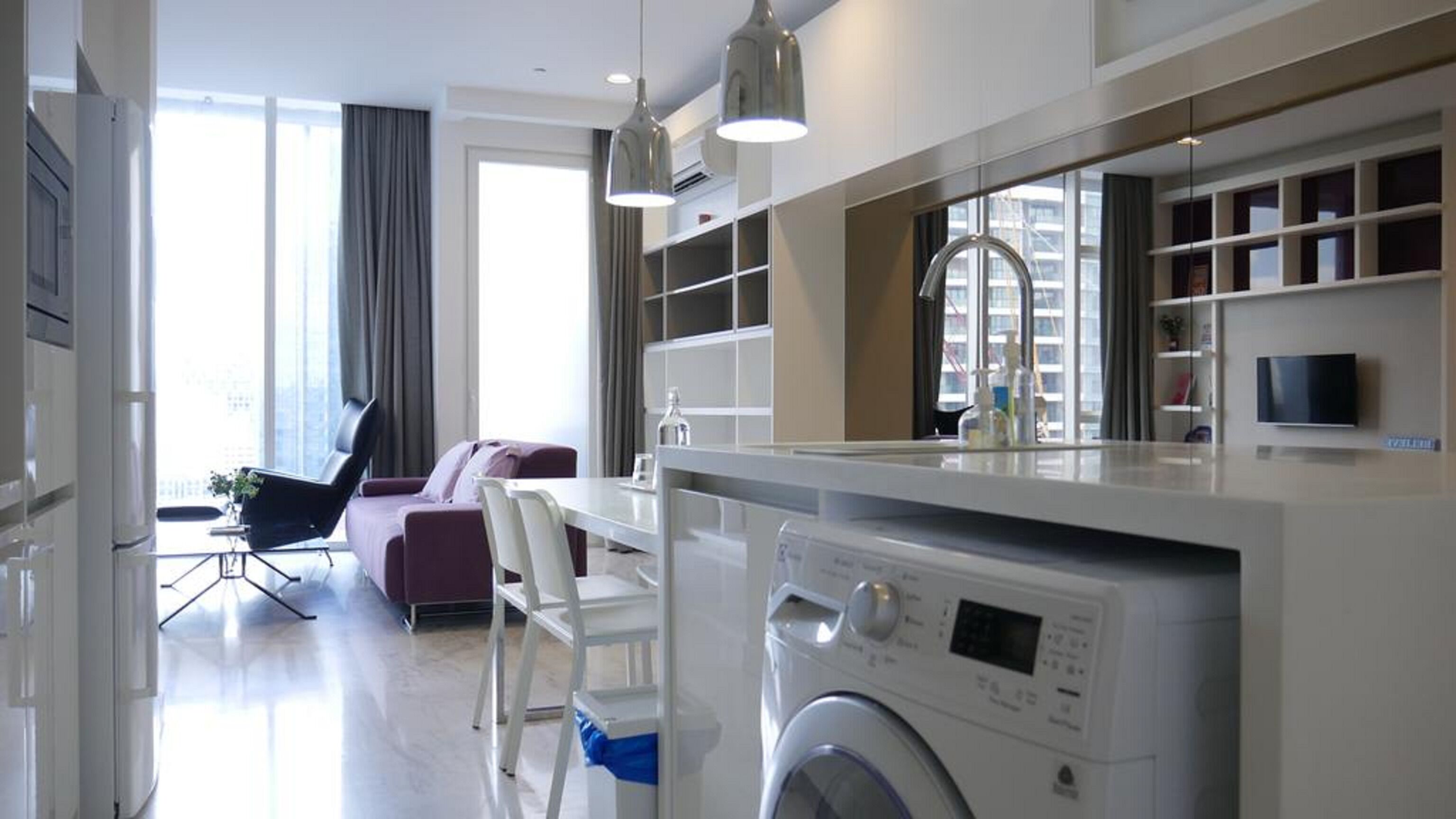 Una cocina moderna con lavadora integrada, un área de comedor con sofá y un amplio ventanal que proporciona luz natural.