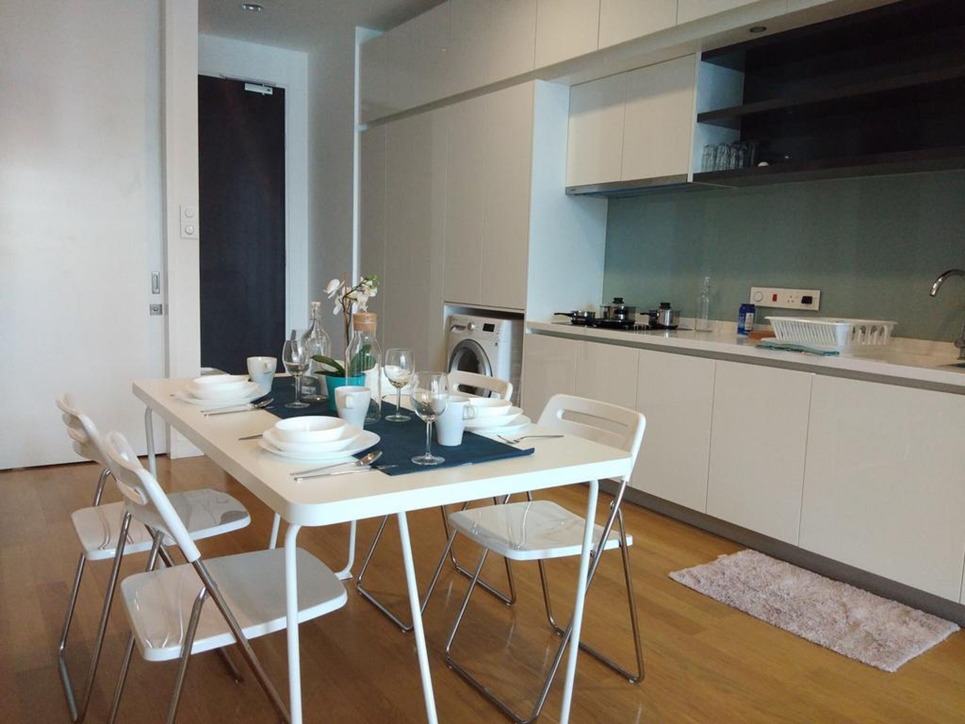 A modern kitchen with white cabinets, a dining table set with plates, glasses, and a vase with flowers.