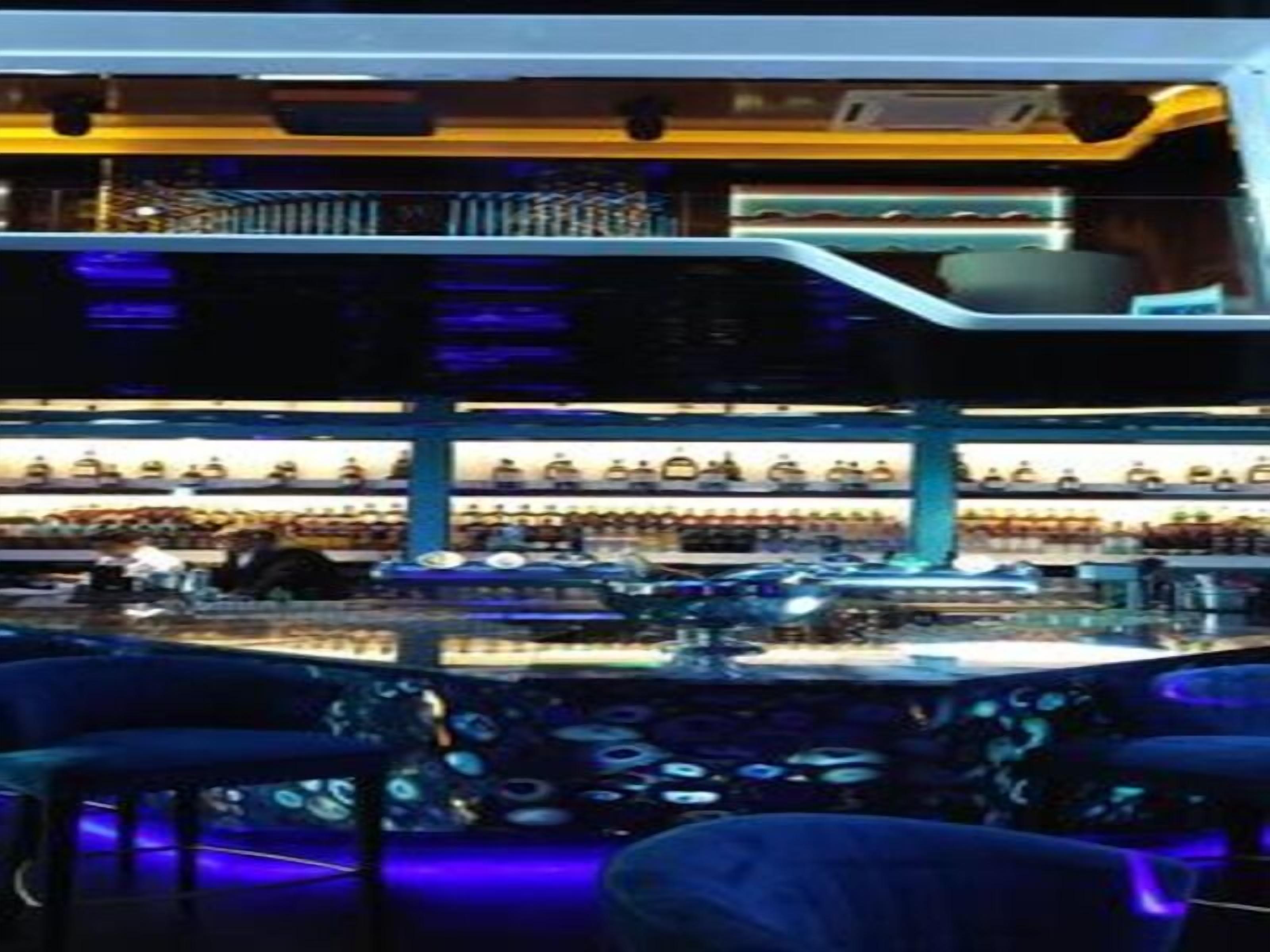 A bar area with a counter, stools, and shelves with bottles.