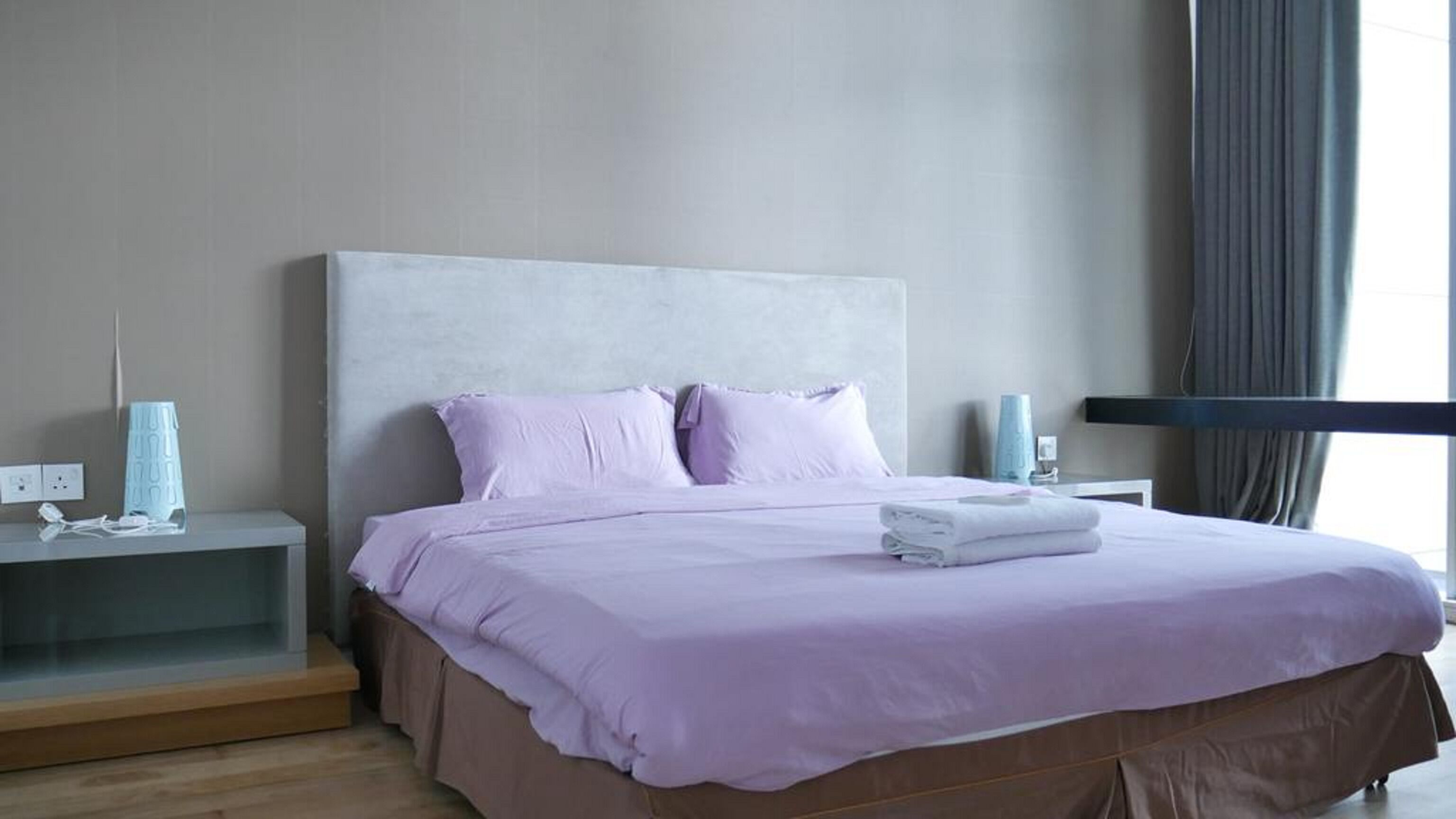 A modern bedroom with a large bed, a nightstand, a lamp, and a window with curtains.