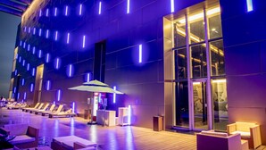 Un hall d’hôtel moderne avec un espace piscine, des chaises longues et un comptoir d’accueil.