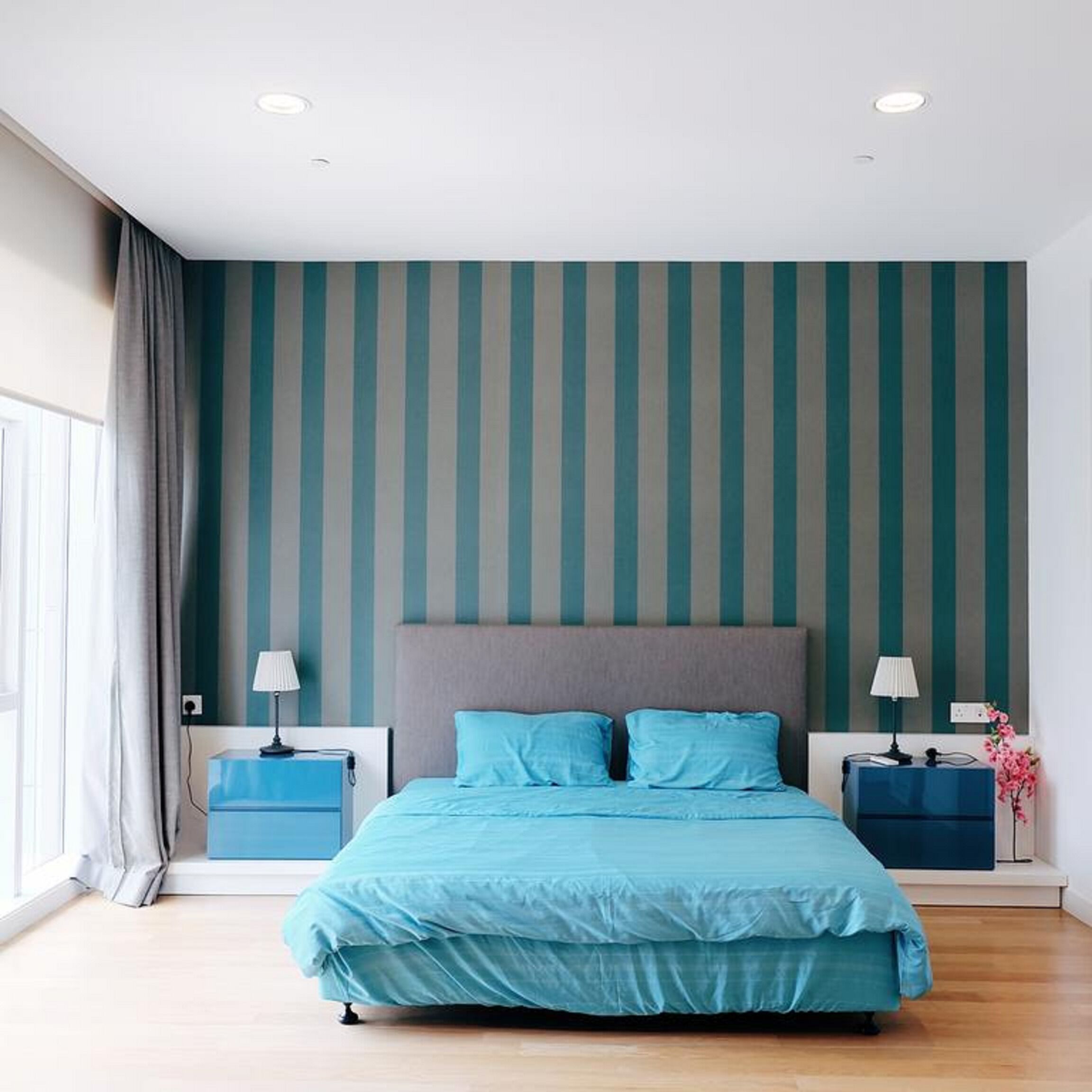 A modern bedroom with a large bed, two bedside tables, and a striped wall.